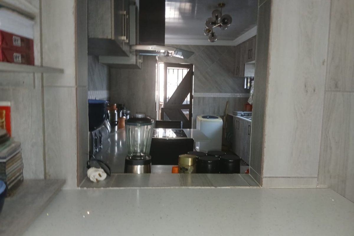 A view through a serving hatch into a kitchen featuring built-in cabinetry, stone countertops, and a modern extractor fan.