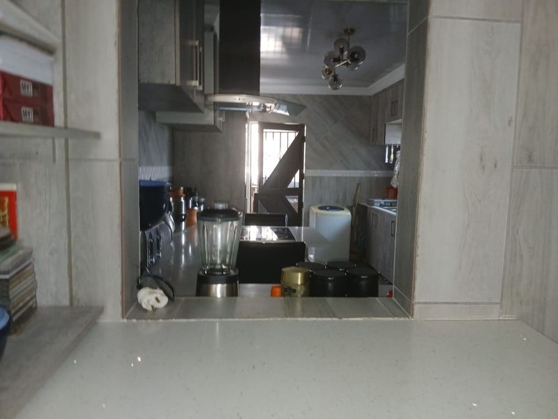 A view through a serving hatch into a kitchen featuring built-in cabinetry, stone countertops, and a modern extractor fan.