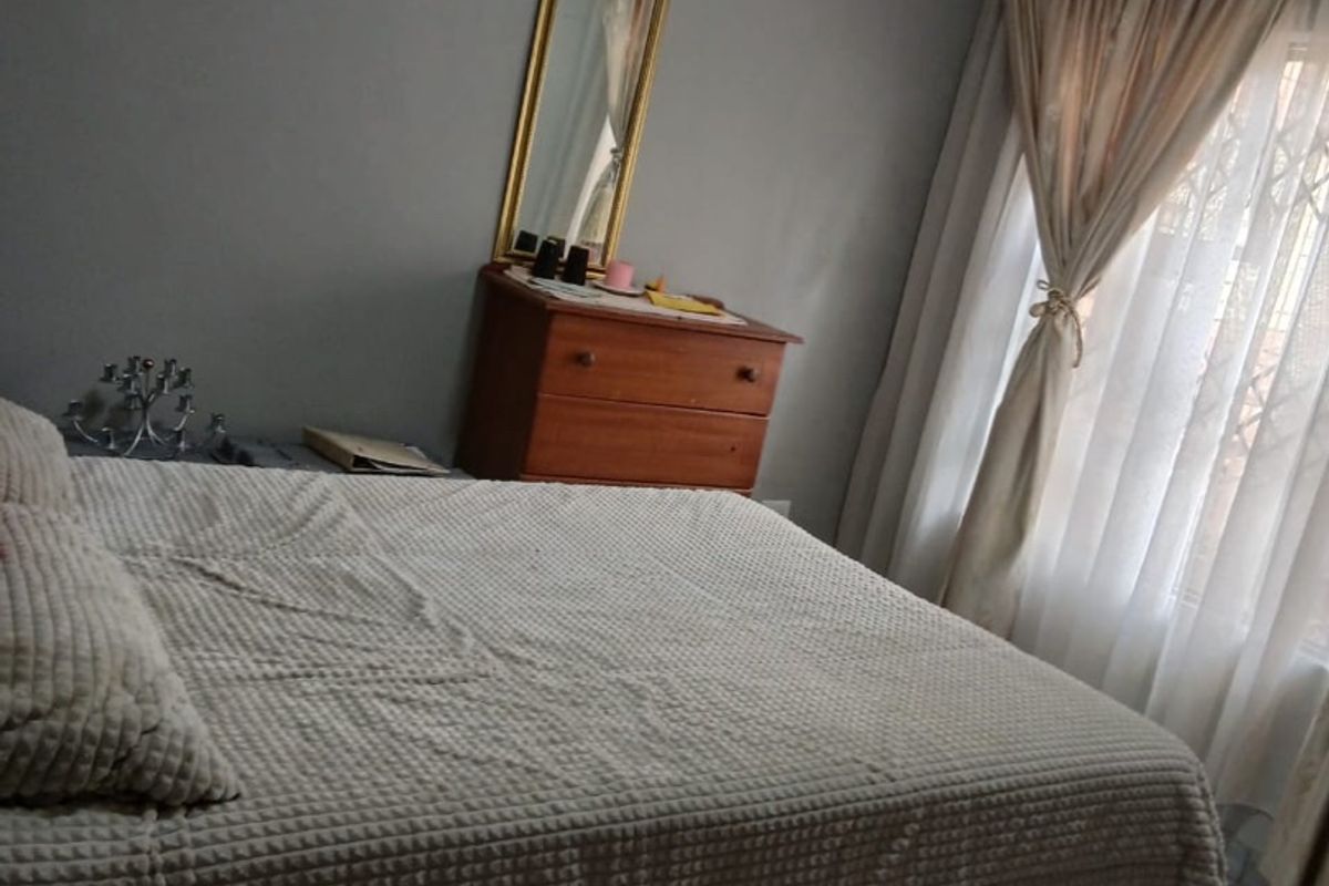 A functional bedroom featuring tiled flooring, neutral wall finishes, and a window fitted with a security gate and curtains.