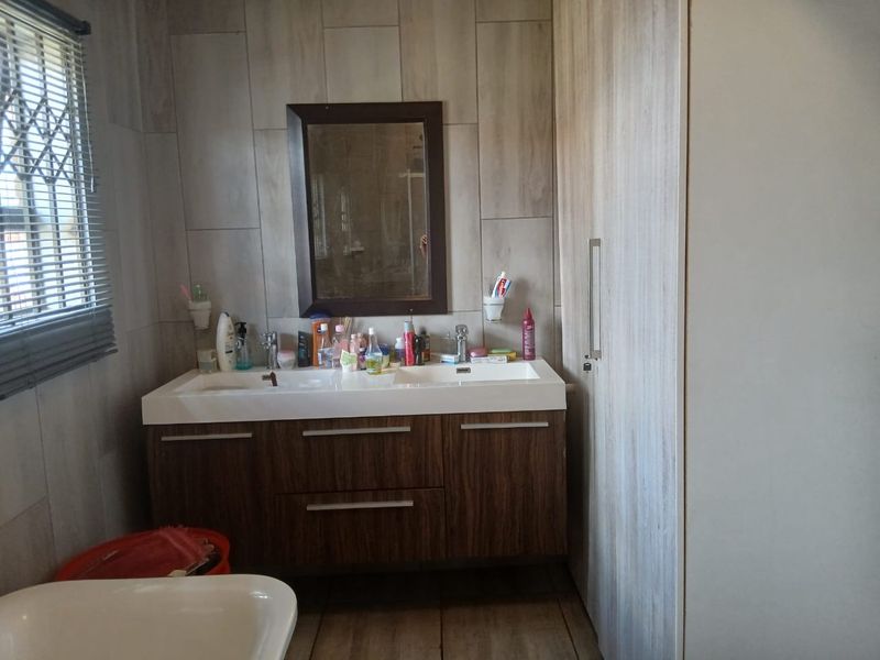 A functional bathroom featuring a modern double vanity with built-in cabinetry, wall-mounted mirror, and neutral tiled wall finishes.