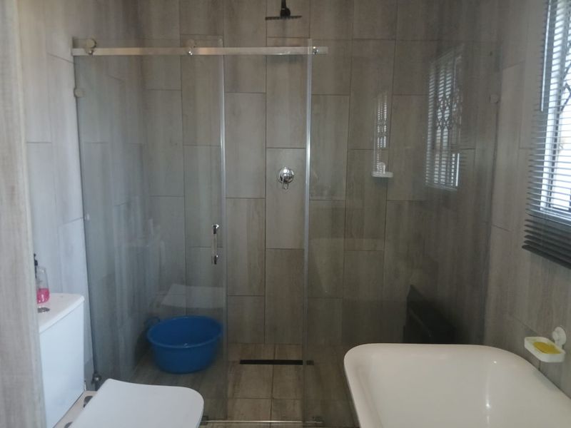 Modern bathroom featuring a walk-in shower with a glass screen, rain shower head, and contemporary wall and floor tiling.