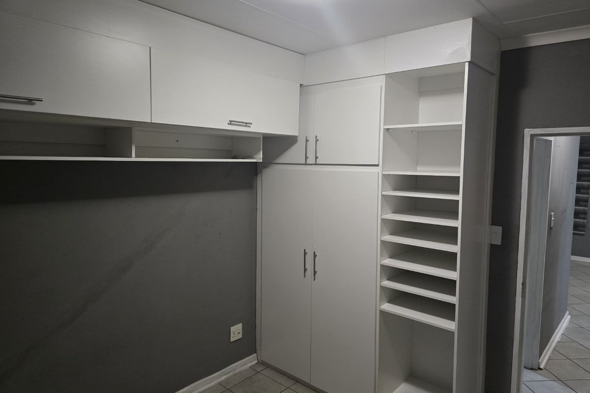 A clean, empty bedroom featuring white built-in cupboards with integrated shelving and neutral tiled flooring.
