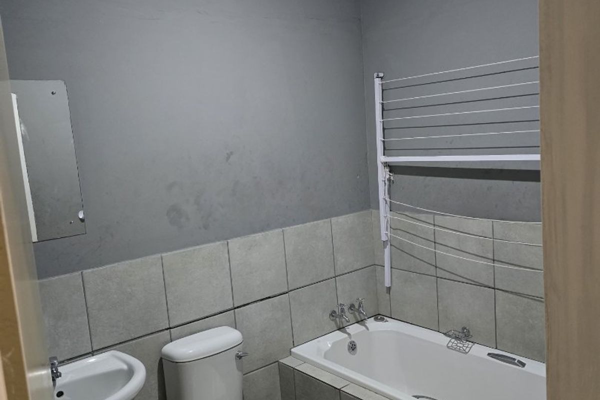 A functional bathroom featuring a pedestal basin, toilet, and bathtub with tiled finishes. The space is clean but would benefit from a cosmetic refresh.