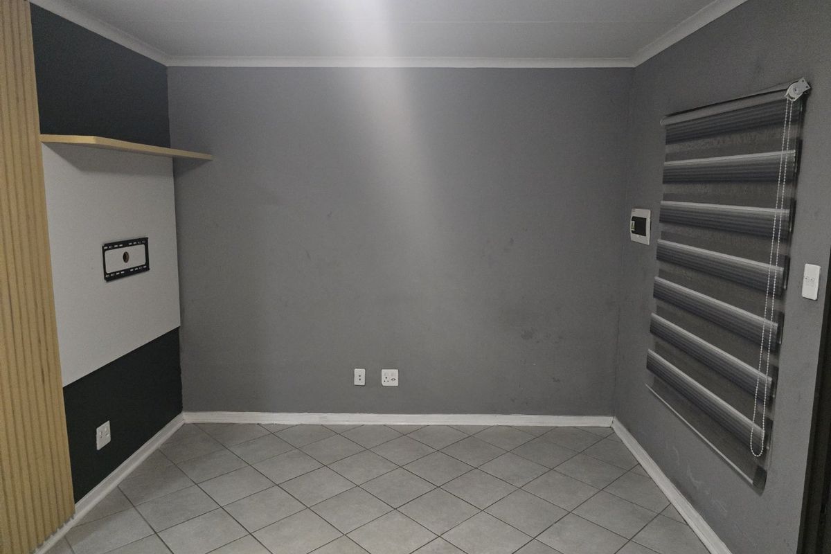 An empty living room featuring tiled flooring, neutral grey walls, built-in shelving, and modern roller blinds, ready for personalization.