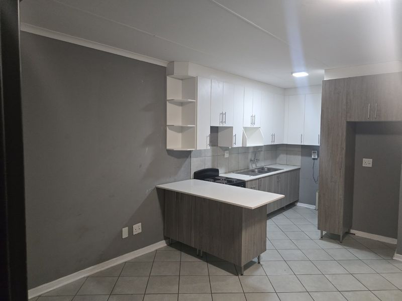 A functional kitchen featuring modern two-tone cabinetry, tiled flooring, a breakfast counter, and a tiled backsplash, offering a clean and practical workspace.