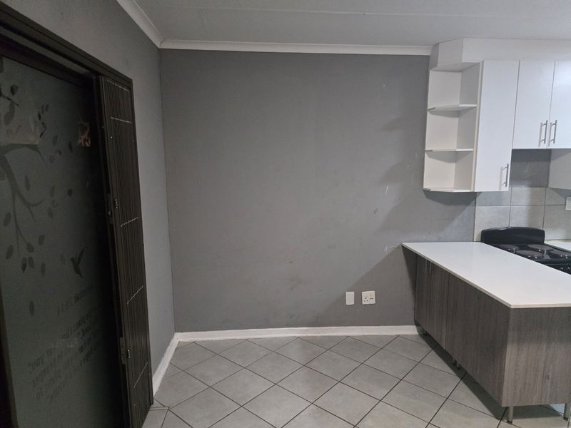 A functional kitchen area featuring built-in cabinetry, open shelving, a hob, and tiled flooring, presenting a clean, empty space ready for personalization.