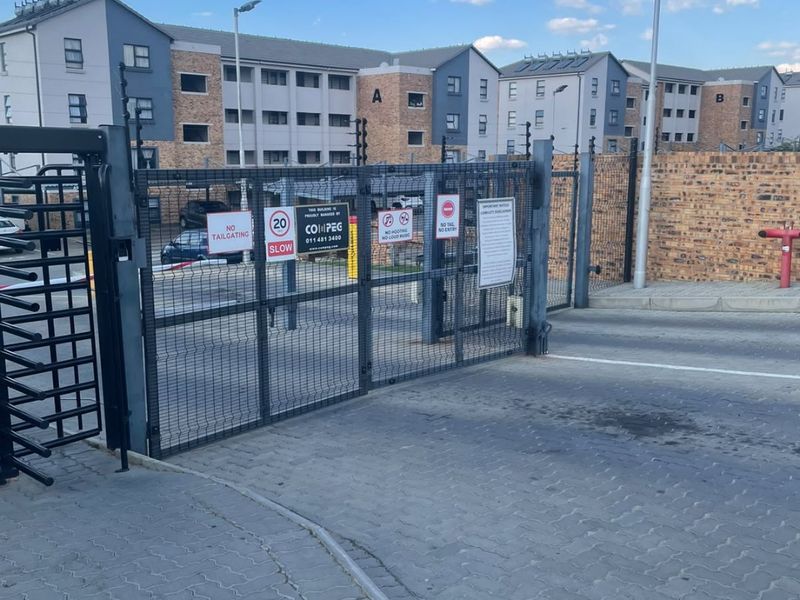 Secure gated entrance to the apartment complex featuring paved driveway, perimeter brick walling, and electric fencing for enhanced security.