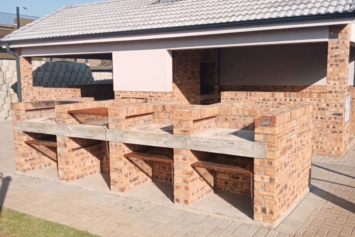 A well-maintained outdoor entertainment area featuring a substantial brick-built braai station with multiple grills, a chimney, and a paved patio.