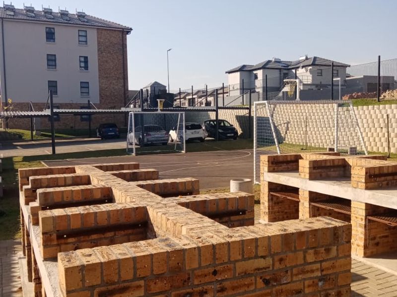 Outdoor communal area featuring brick braai facilities, paved ground, and a small sports court with goal posts within a residential complex.
