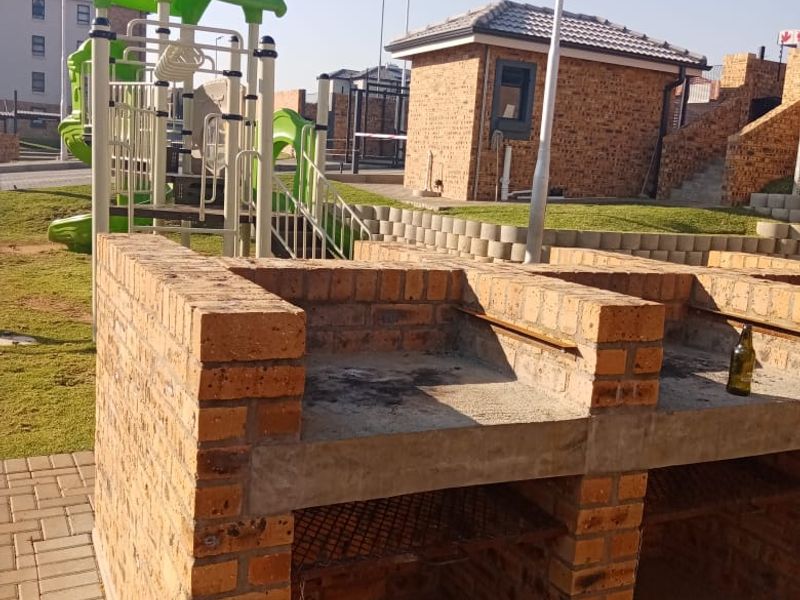 Outdoor communal area featuring a built-in brick braai facility and adjacent playground equipment within a residential apartment complex.
