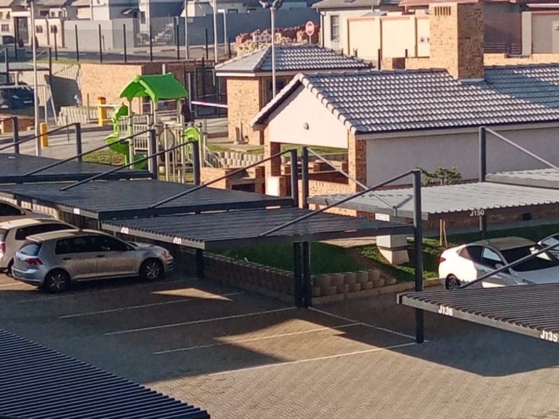 An elevated view of the apartment complex parking area featuring covered carports, paved surfaces, and communal playground facilities.
