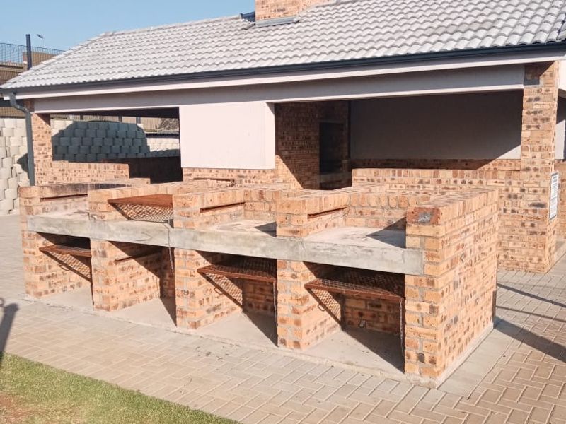 A well-maintained outdoor entertainment area featuring a substantial brick-built braai station with multiple grills, a chimney, and a paved patio.