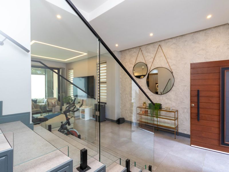 Modern entrance hall featuring a sleek glass balustrade, tiled flooring, and a solid wood front door with contemporary textured wall finishes.