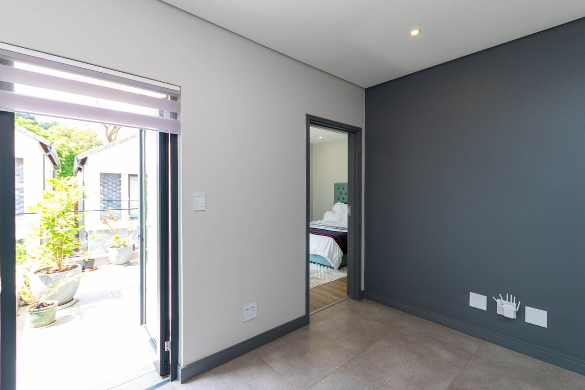 A bright, modern bedroom featuring neutral and charcoal accent walls, tiled flooring, and direct access to an outdoor balcony area.