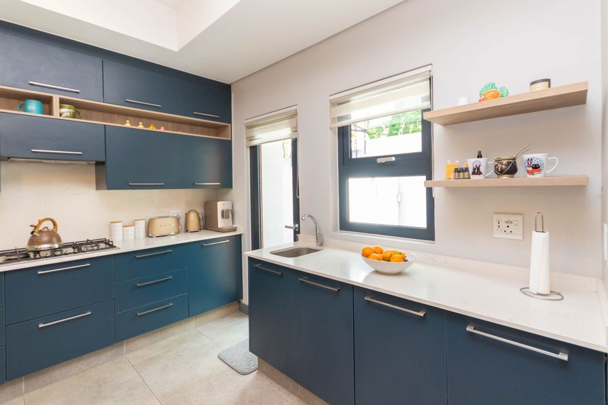 Modern kitchen featuring dark blue cabinetry, stone countertops, gas hob, and floating shelves, offering a clean and contemporary aesthetic.