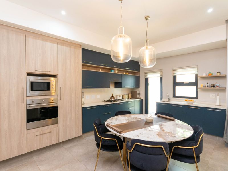 Modern open-plan kitchen featuring two-tone cabinetry, stone countertops, integrated appliances, and a dedicated dining area with stylish pendant lighting.