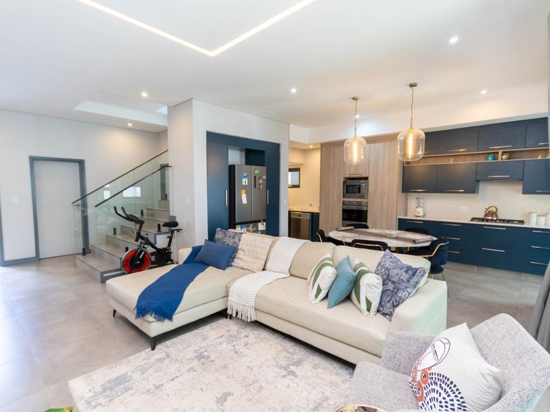 Modern open-plan living area featuring a contemporary kitchen with dark blue cabinetry, integrated appliances, and a seamless transition to the staircase with glass balustrade.