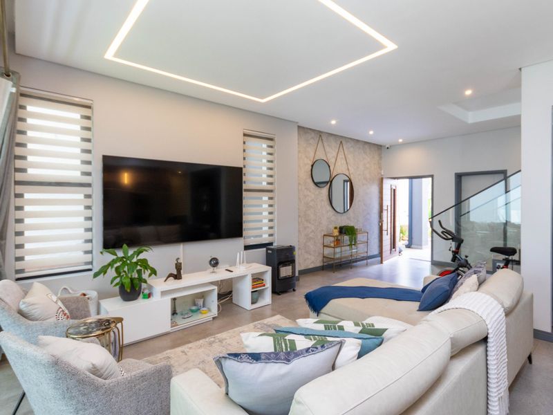 Modern living room featuring a textured feature wall, recessed square ceiling lighting, tiled floors, and a glass balustrade staircase.