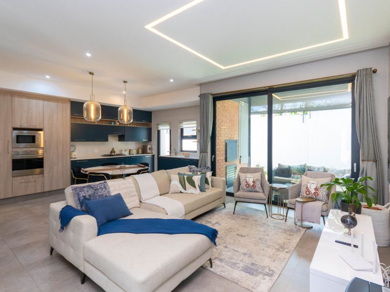 Modern open-plan living area featuring a sleek kitchen with integrated appliances, recessed ceiling lighting, and large sliding doors leading to an outdoor patio.