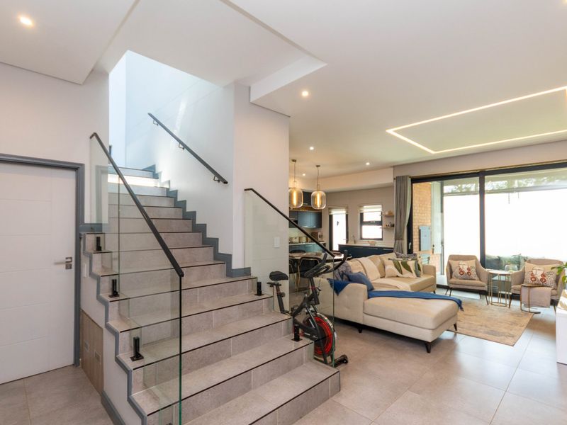 Modern open-plan living area featuring a tiled staircase with glass balustrade, recessed ceiling lighting, and large sliding doors leading to the outdoor space.