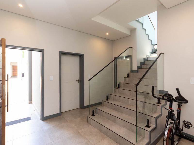 Modern entrance hall featuring a contemporary staircase with glass balustrades, tiled flooring, and recessed lighting, providing a clean and bright welcome to the home.