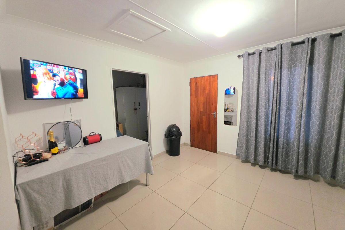 A functional living area featuring neutral tiled flooring, a timber door, and a ceiling access hatch, providing a clean and simple living space.
