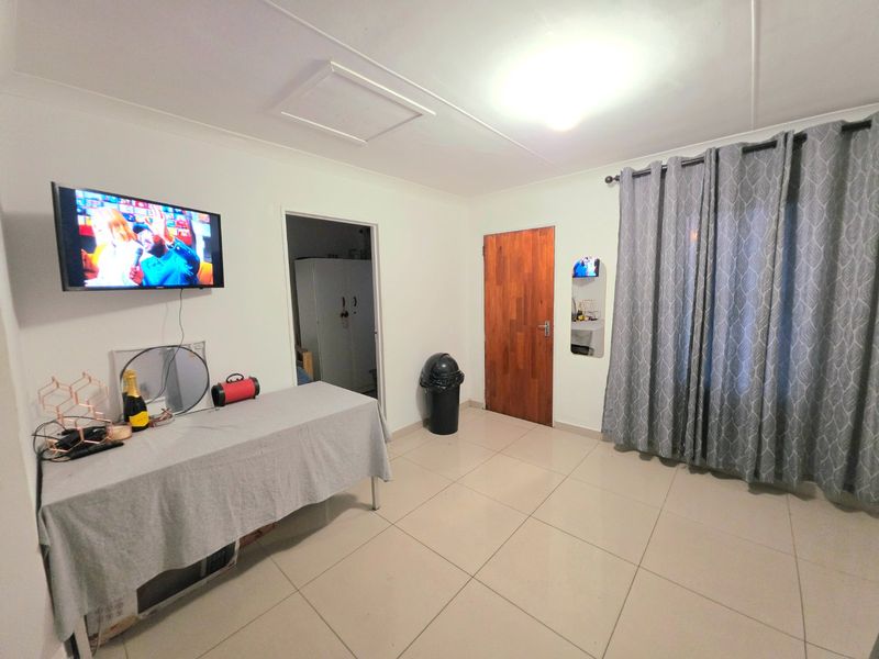 A functional living area featuring neutral tiled flooring, a timber door, and a ceiling access hatch, providing a clean and simple living space.