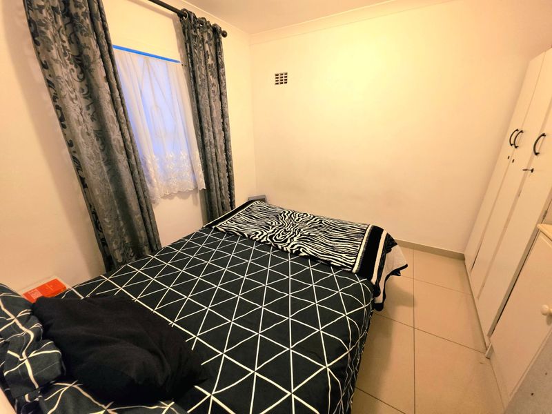 A functional bedroom featuring tiled flooring, a built-in wardrobe, and a ventilation brick, providing a clean and practical living space.