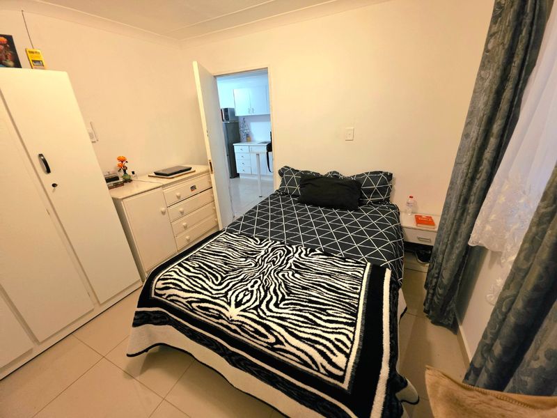 A functional bedroom featuring tiled flooring, a built-in wardrobe, and direct access to an adjacent kitchen area.