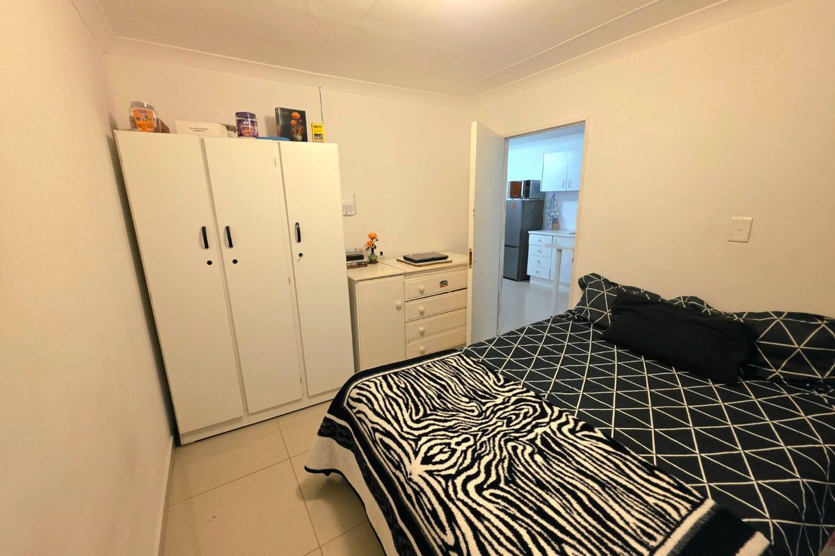 A functional bedroom featuring tiled flooring and coved ceilings, with a view into the adjacent kitchen area.