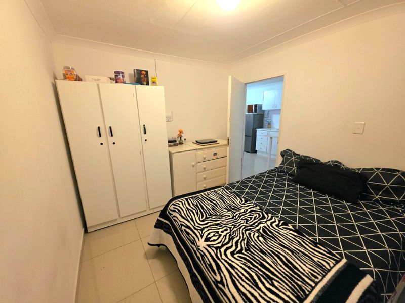 A functional bedroom featuring tiled flooring and coved ceilings, with a view into the adjacent kitchen area.