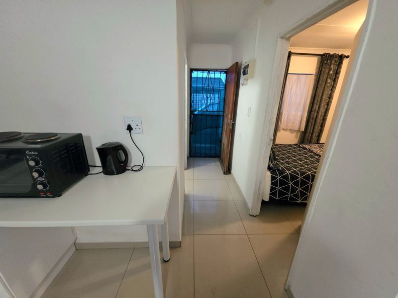 A functional hallway with tiled flooring, providing access to an adjacent bedroom and an exterior security door.