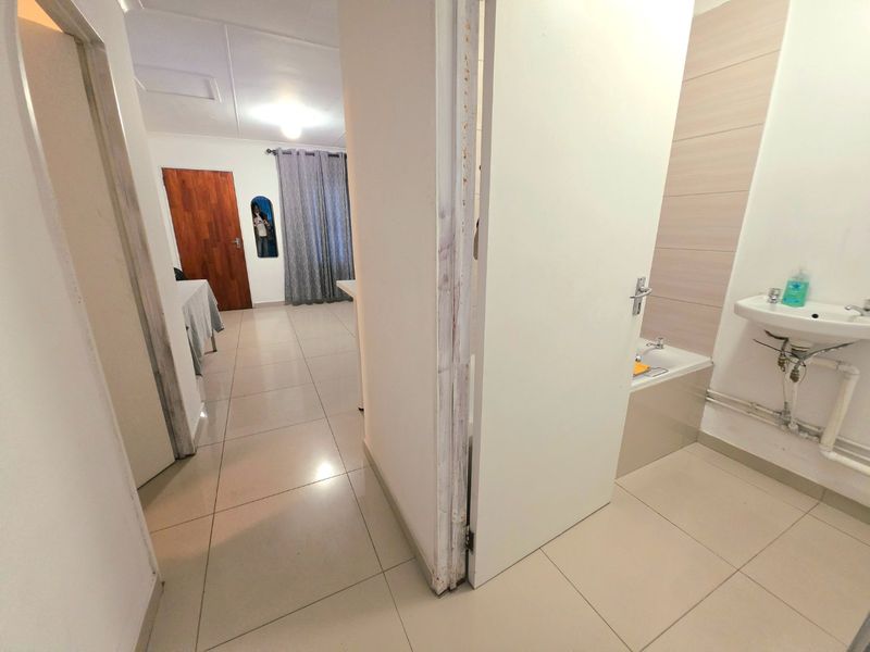 A hallway view showing tiled flooring leading to a bedroom and an adjacent bathroom with a vanity and bathtub.