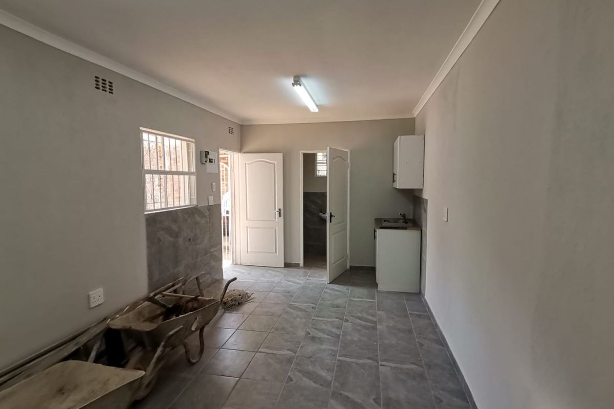 A functional, empty kitchen area featuring tiled flooring, basic cabinetry with a sink, and security bars on the window.