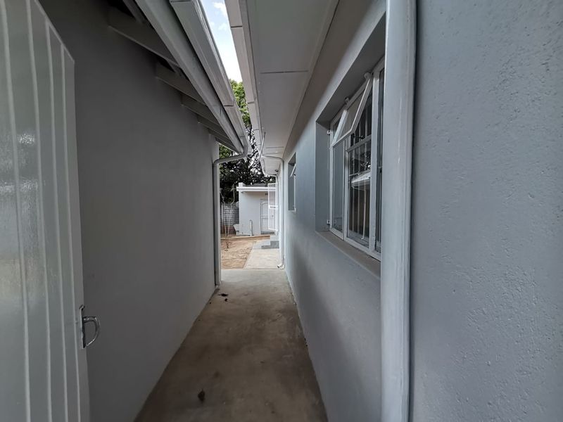 A narrow exterior side passage featuring concrete flooring, guttering, and security bars on the windows, leading towards the rear of the property.