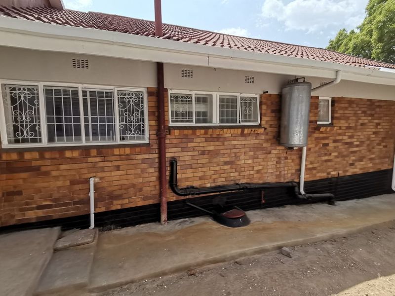 Rear exterior view of the commercial property featuring brick facade, tiled roof, security bars on windows, and external plumbing infrastructure.