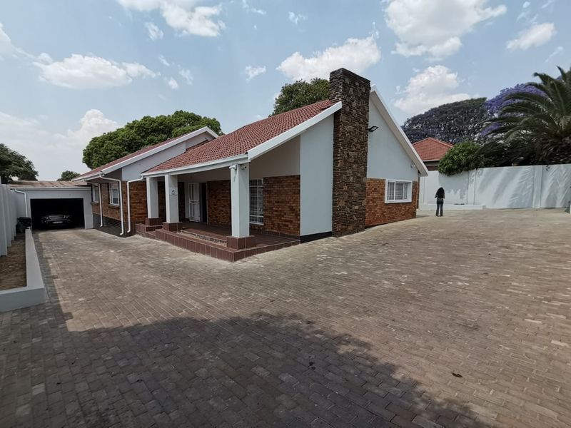 A well-maintained commercial property featuring a brick facade, tiled roof, stone chimney, and a spacious paved driveway leading to a garage.