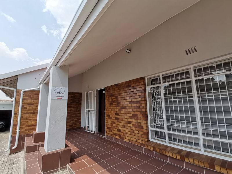 Front entrance area of a commercial property featuring a covered tiled patio, brick facade, and secure window bars.