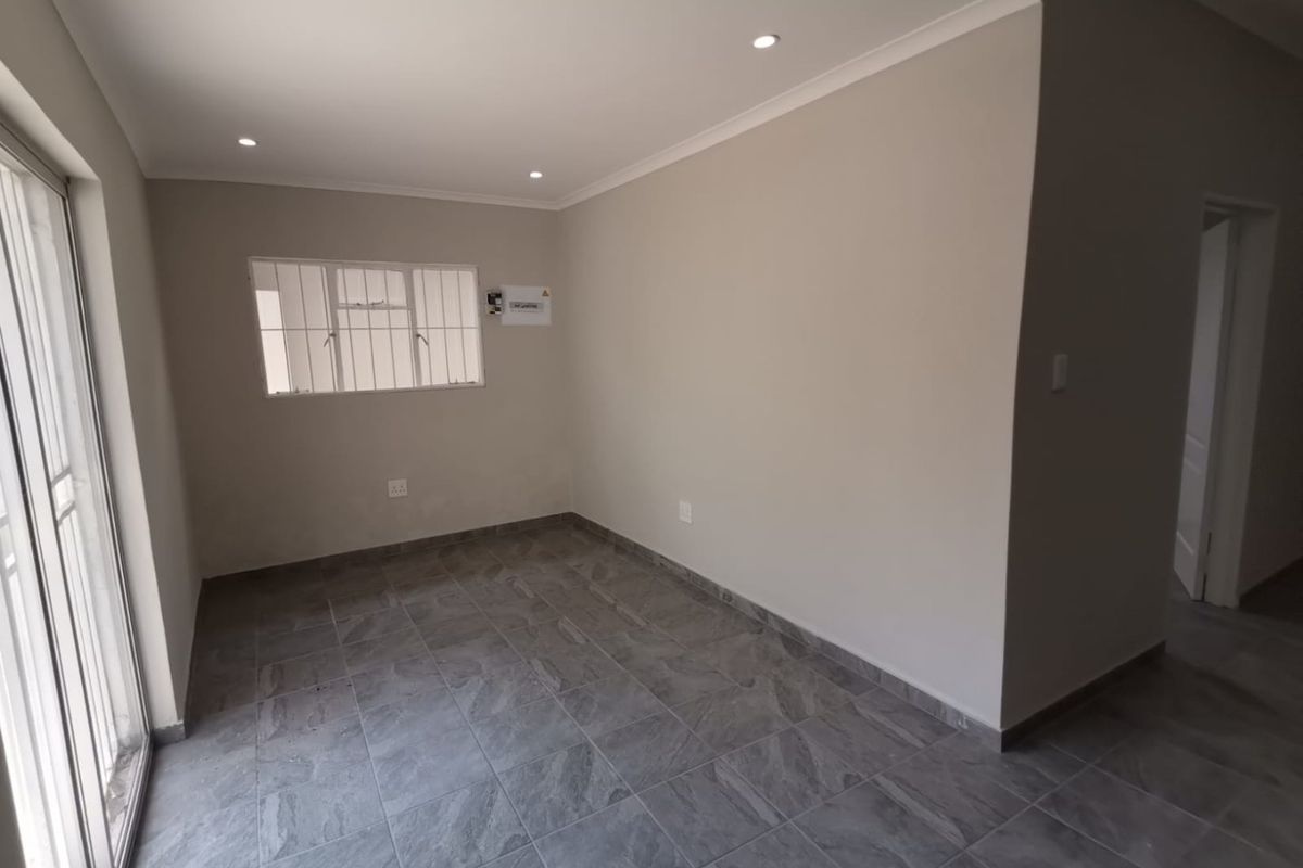 A bright, empty living area featuring modern grey tiled flooring, recessed downlights, and a sliding glass door providing natural light.