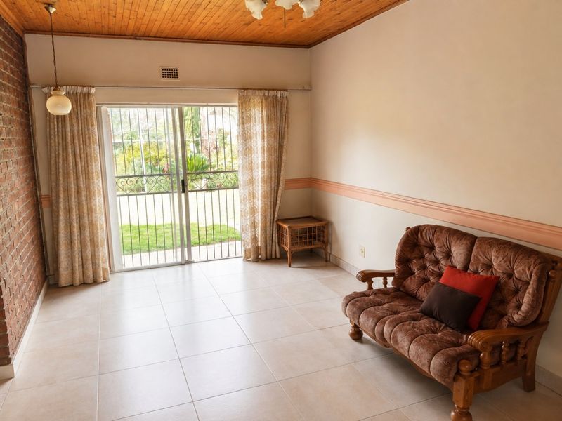 Living room featuring a timber ceiling, exposed brick wall, ceramic floor tiles, and sliding glass doors providing direct access to the garden.
