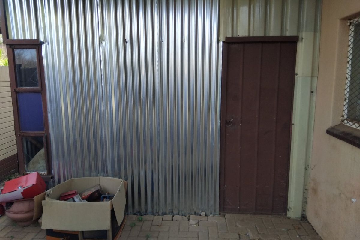 Rear exterior view featuring corrugated metal wall cladding, a steel door, and paved patio area.