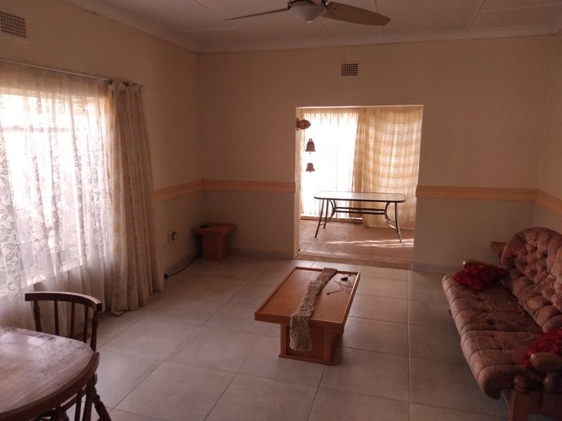 A spacious living area featuring tiled flooring, a ceiling fan, and a transition to an adjacent sunroom through a sliding glass door.