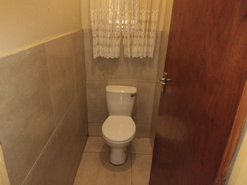 A compact guest bathroom featuring neutral ceramic wall and floor tiles and a standard white toilet.