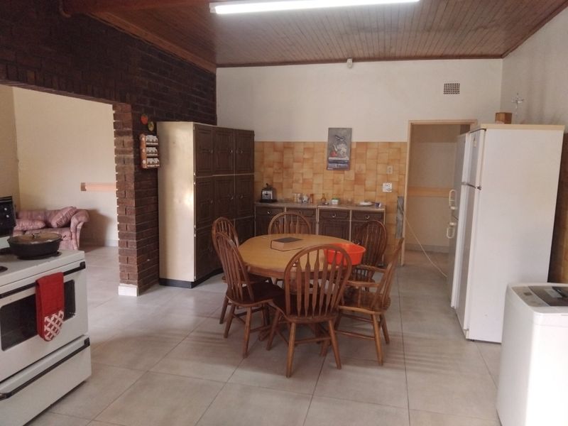 Open plan kitchen and dining area featuring exposed brickwork, timber ceiling, and tiled flooring with dated cabinetry and finishes.