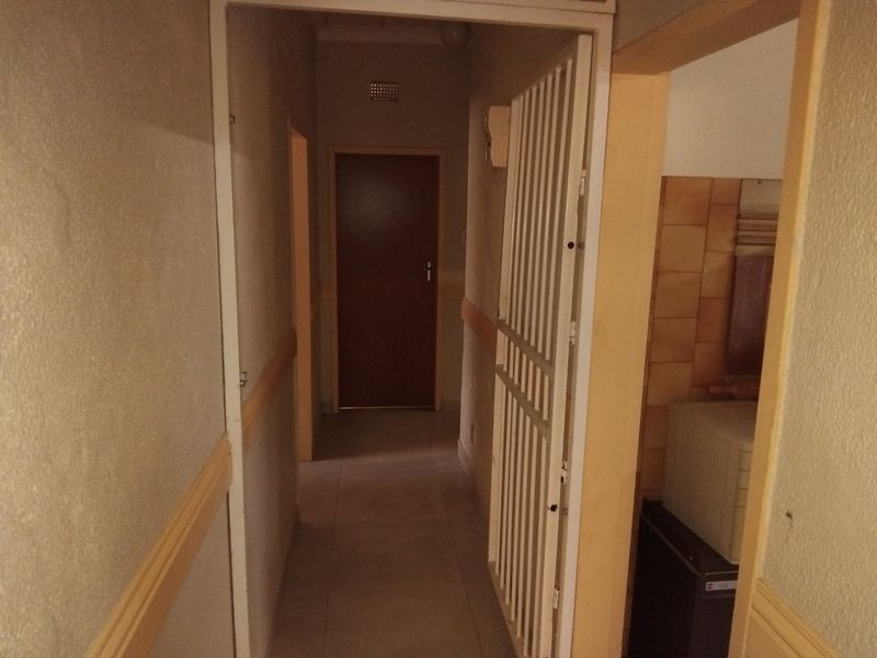 A narrow interior hallway featuring tiled flooring, a security gate, and dated wall finishes, providing access to adjacent rooms.