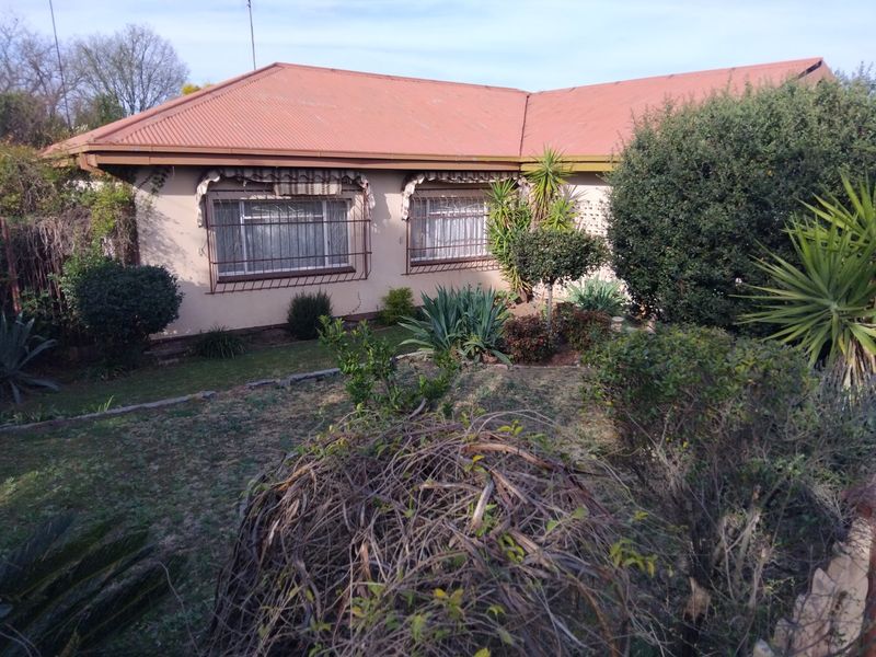 Front elevation of a single-story house featuring a corrugated metal roof, security window bars, and established garden landscaping.