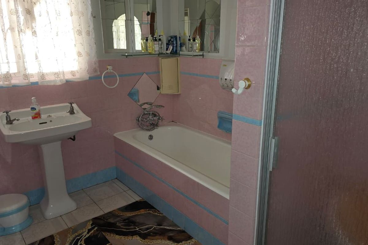 A dated bathroom featuring a pedestal basin, built-in bathtub, and shower enclosure with original pink and blue wall tiling.