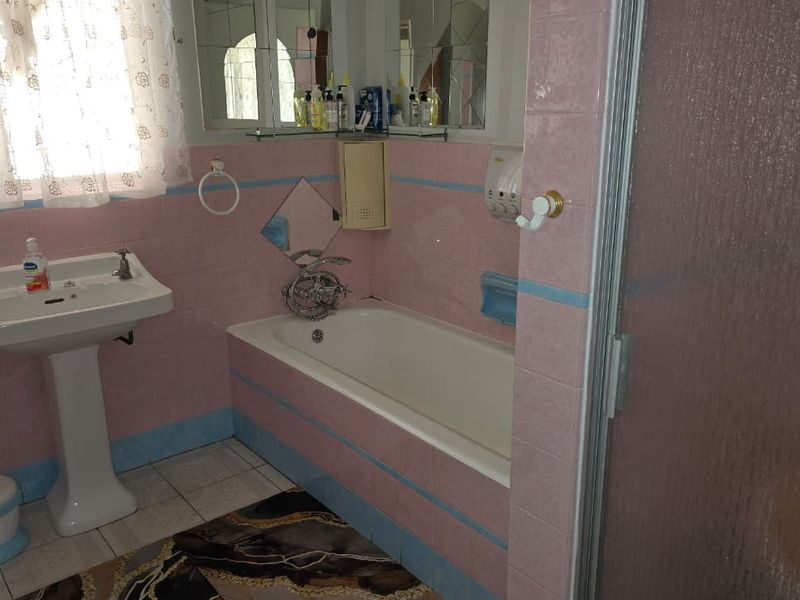 A dated bathroom featuring a pedestal basin, built-in bathtub, and shower enclosure with original pink and blue wall tiling.