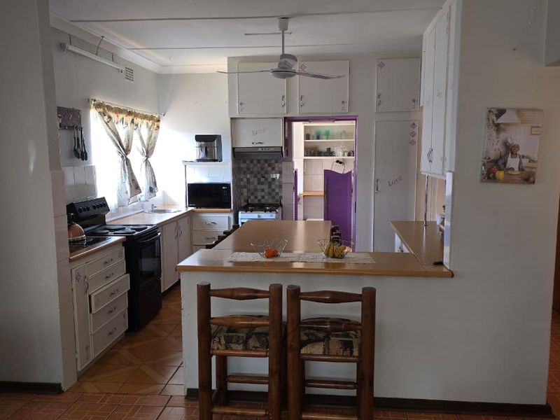A functional kitchen featuring built-in cabinetry, laminate countertops, a freestanding stove, and tiled flooring, with an adjacent scullery area.