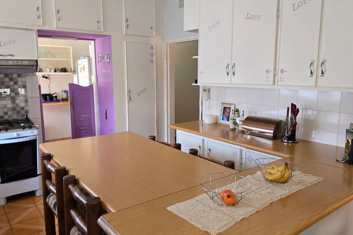A dated kitchen featuring built-in cabinetry, laminate countertops, and a gas stove, with an adjacent scullery area visible through the doorway.